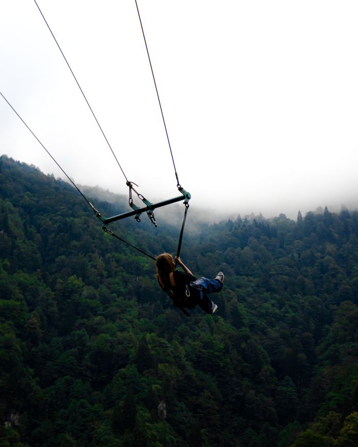 Silhouette of a person on a swing over lush green forest in Rize, Türkiye. Perfect for adventure themes.