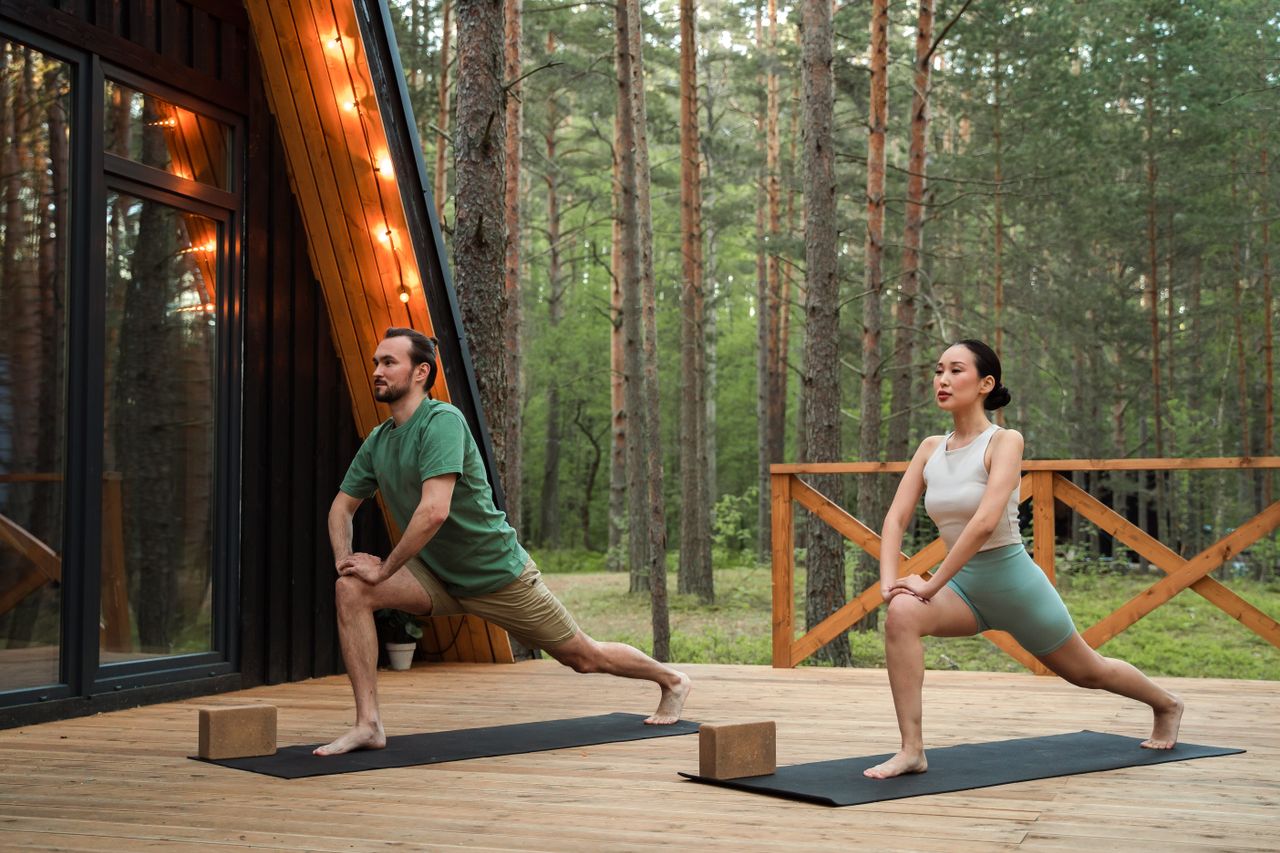 A couple performs yoga stretches on a forest deck, promoting fitness and relaxation.